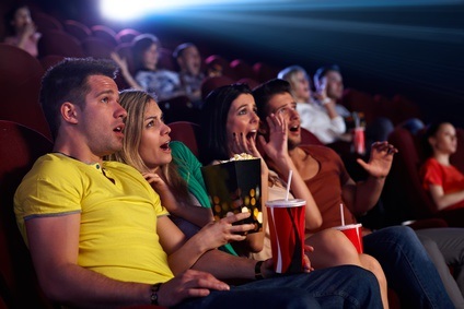 Audience sitting in multiplex movie theater, watching horror movie, screaming.